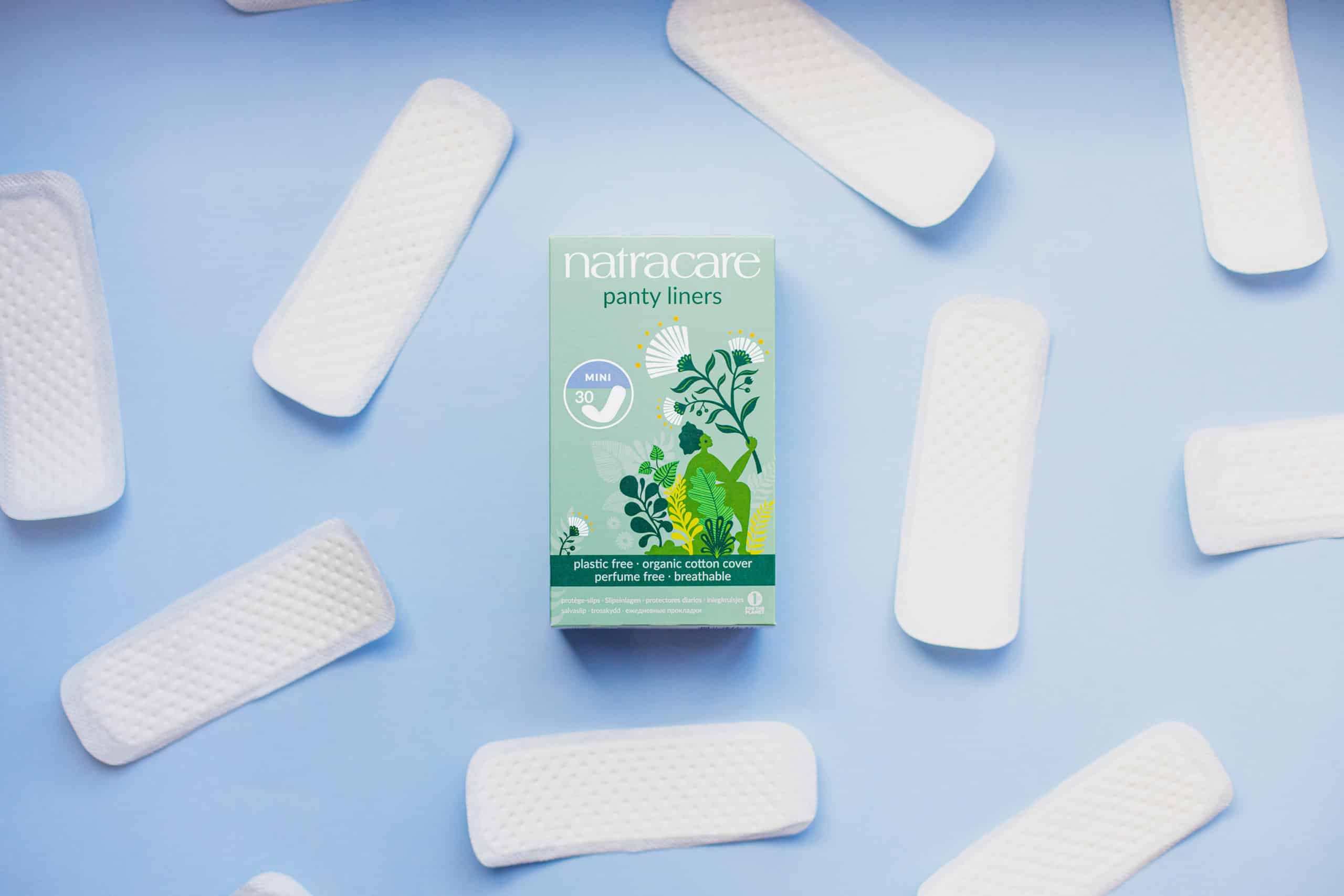 Ein Bild aus dem Taiga Store von taiga.green. Eine Schachtel mit Natracare-Slipeinlagen von Taiga.green eco living steht auf einem blauen Hintergrund, umgeben von mehreren einzeln ausgelegten Slipeinlagen. Die Schachtel zeigt grünes Blattwerk und Produktinformationen. Jetzt bestellen im Eco Shop von www.taiga.green. Hier nachhaltig einkaufen mit dem Taiga Eco Rating