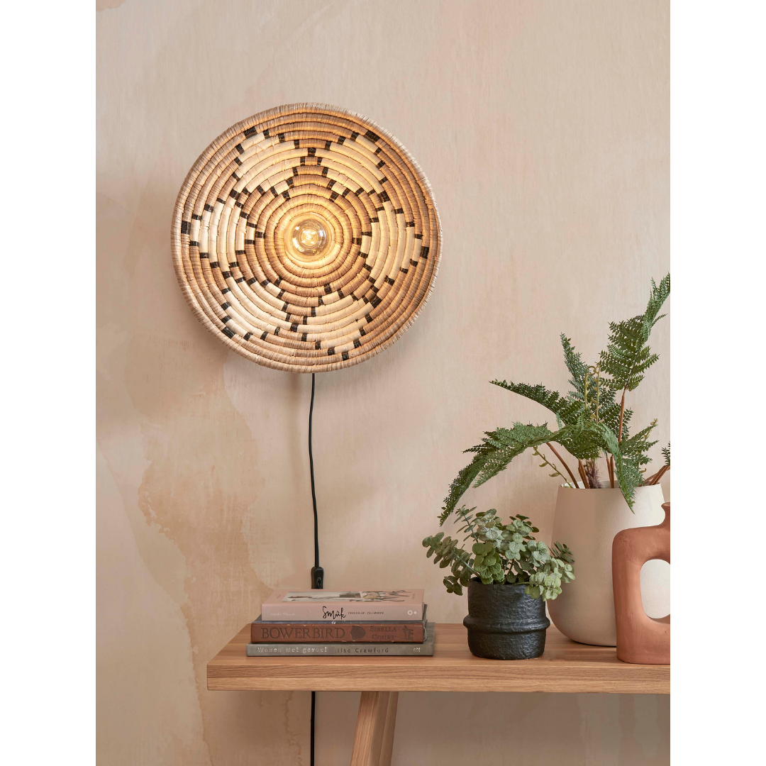 Ein Bild aus dem Taiga Store von taiga.green. Die Wandlampe Andros Diam.45x8cm leuchtet über einem Holztisch, der mit gestapelten Büchern, Topfpflanzen und einem Terrakotta-Ornament vor einer neutral getönten Wand dekoriert ist. Jetzt bestellen im Eco Shop von www.taiga.green. Hier nachhaltig einkaufen mit dem Taiga Eco Rating
