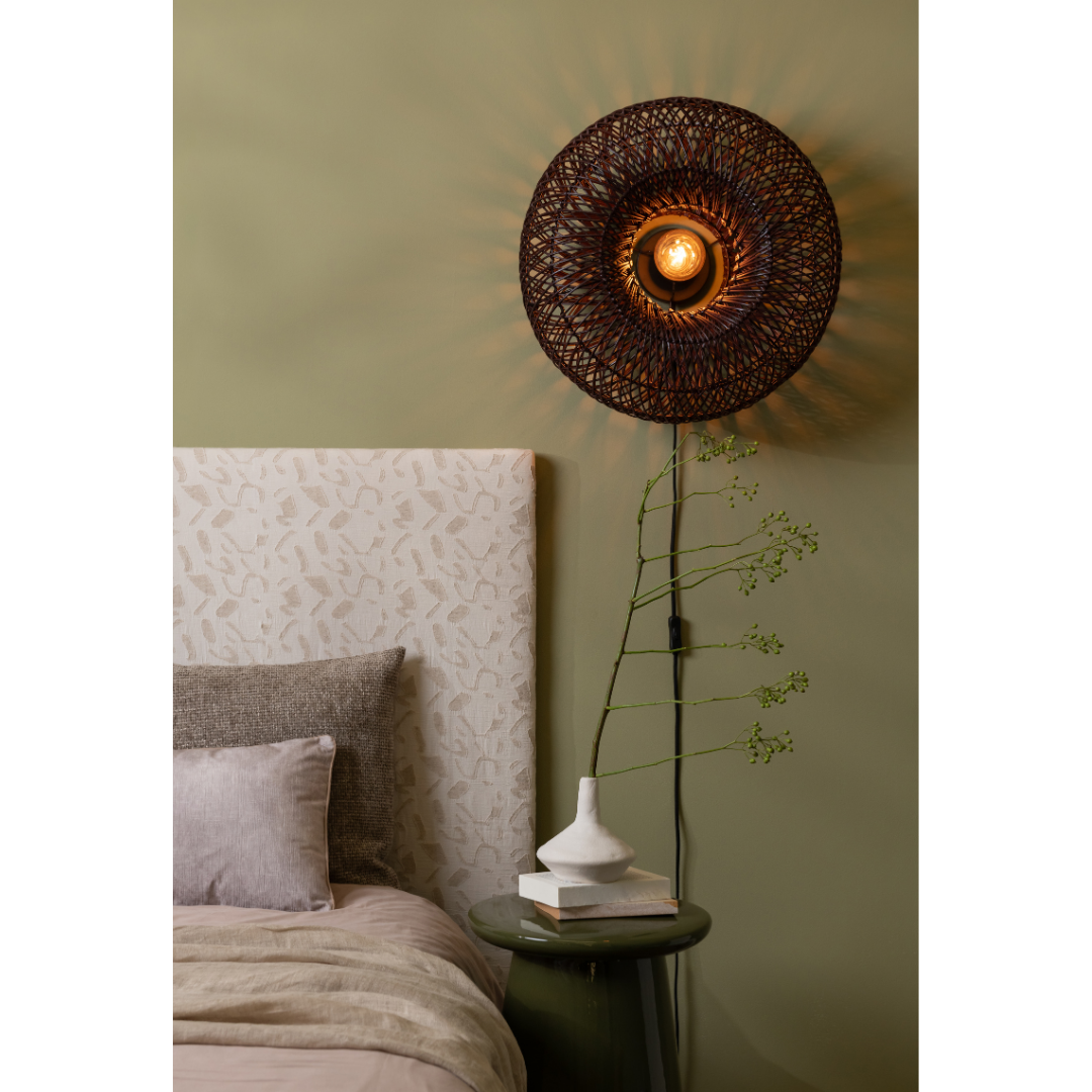 Ein Bild aus dem Taiga Store von taiga.green. Eine gemütliche Schlafzimmerecke mit einem gemusterten Kopfteil, einem aufgeräumten Bett, einem runden grünen Beistelltisch und der Wandlampe Arizona Rattan/Schirm ø50x23cm S, die warmes Licht auf eine grüne Wand wirft. Jetzt bestellen im Eco Shop von www.taiga.green. Hier nachhaltig einkaufen mit dem Taiga Eco Rating