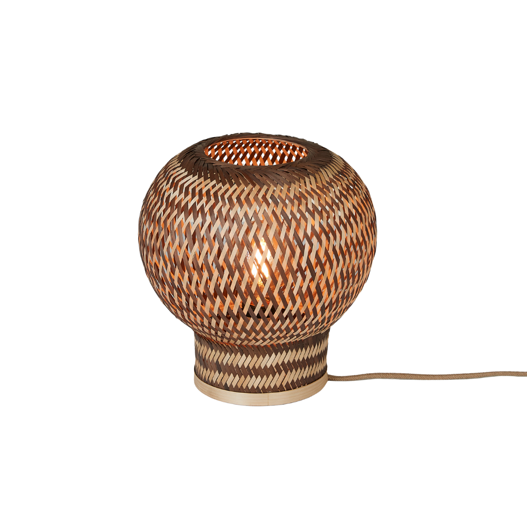 Ein Bild aus dem Taiga Store von taiga.green. Die Tischlampe Barbados Bambus/Globe ø25xh.27cm ist eine runde, geflochtene Rattan-Tischlampe mit Chevron-Muster und warmem Lichtschein, die auf einem leichten, runden Sockel steht, von dem ein elektrisches Kabel ausgeht. Jetzt bestellen im Eco Shop von www.taiga.green. Hier nachhaltig einkaufen mit dem Taiga Eco Rating