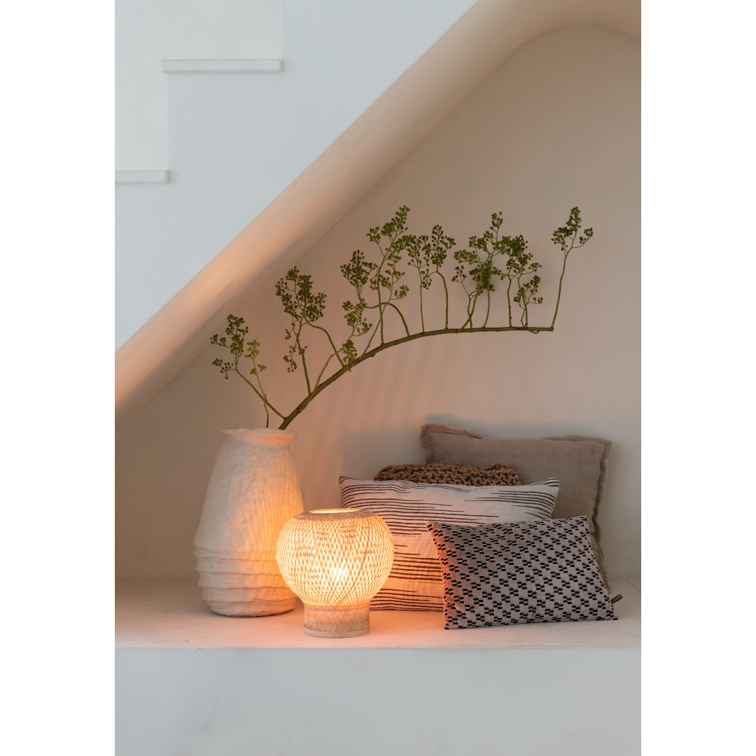 Ein Bild aus dem Taiga Store von taiga.green. In einer gemütlichen Ecke unter der Treppe sorgen neutrale Kissen, ein gemustertes Kissen, eine strukturierte Vase mit Grünzeug und die Tischlampe Barbados Bambus/Globe ø25xh.27cm für ein warmes Licht und eine ruhige, einladende Atmosphäre. Jetzt bestellen im Eco Shop von www.taiga.green. Hier nachhaltig einkaufen mit dem Taiga Eco Rating