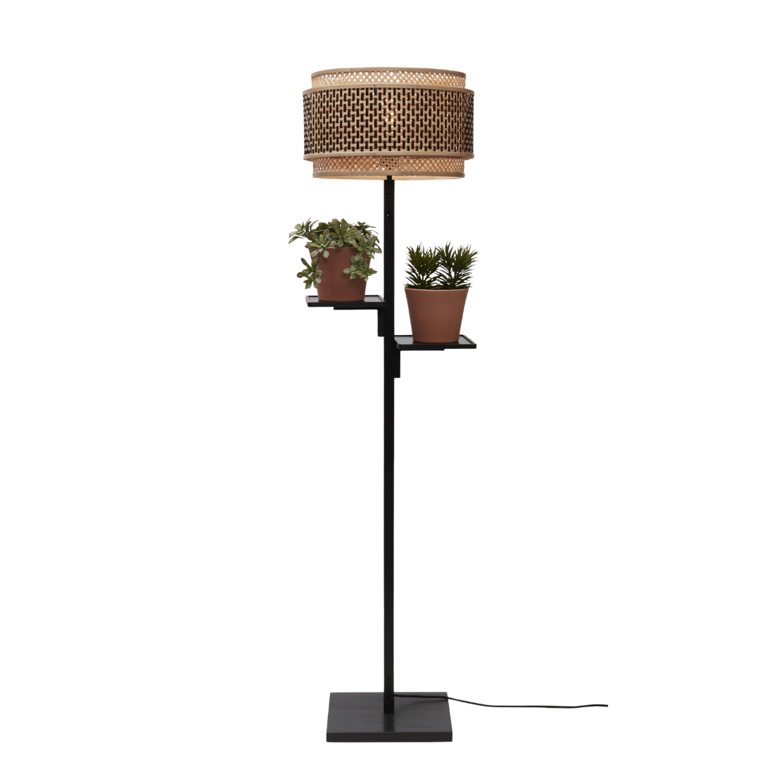 Ein Bild aus dem Taiga Store von taiga.green. Eine moderne Stehlampe mit einem Lampenschirm aus geflochtenem Rattan und zwei kleinen Topfpflanzen auf eingebauten Regalen, die an dem schwarzen Metallständer befestigt sind. Jetzt bestellen im Eco Shop von www.taiga.green. Hier nachhaltig einkaufen mit dem Taiga Eco Rating