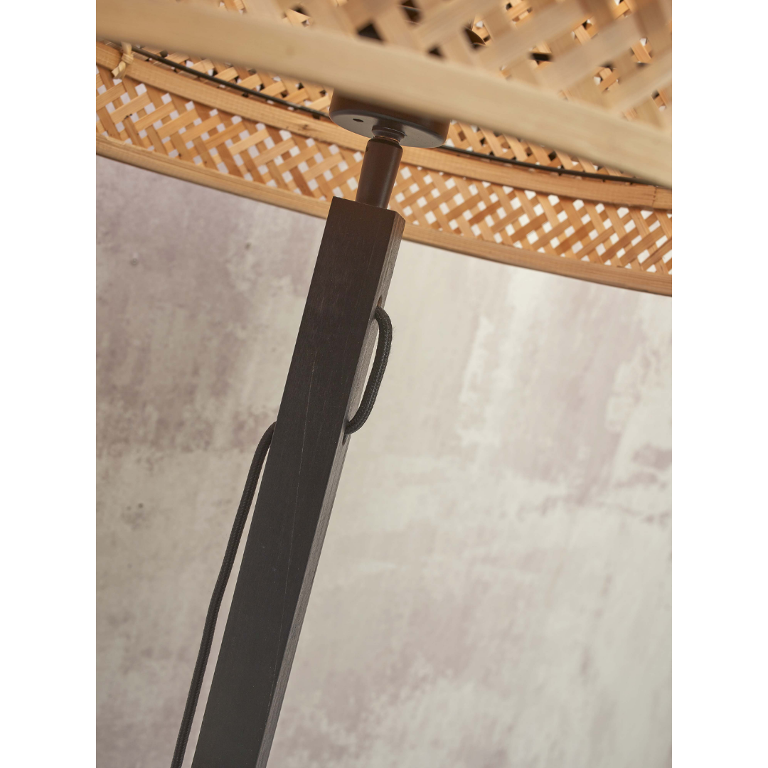 Ein Bild aus dem Taiga Store von taiga.green. Nahaufnahme einer schwarzen Stange, die einen geflochtenen, runden Lampenschirm aus Rattan trägt, wobei eine schwarze Schnur an der Stange entlang läuft. Der Hintergrund ist eine helle, strukturierte Wand. Jetzt bestellen im Eco Shop von www.taiga.green. Hier nachhaltig einkaufen mit dem Taiga Eco Rating