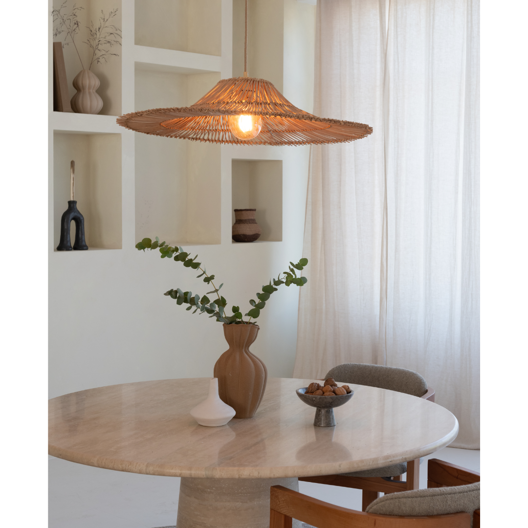Ein Bild aus dem Taiga Store von taiga.green. Ein runder Marmortisch mit einer braunen Vase mit grünen Zweigen, einer kleinen weißen Skulptur und einer Schale steht unter einer geflochtenen Rattan-Pendelleuchte in einem neutralen, minimalistischen Raum mit Einbauregalen und transparenten Vorhängen. Jetzt bestellen im Eco Shop von www.taiga.green. Hier nachhaltig einkaufen mit dem Taiga Eco Rating