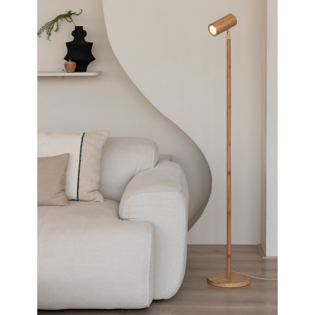 Ein Bild aus dem Taiga Store von taiga.green. Ein modernes Wohnzimmer mit einem hellen Sofa, beigen und hellbraunen Kissen, einer Stehlampe aus Holz und einer weißen Wand mit einem kleinen Regal mit einer schwarzen Vase und einer kleinen Pflanze. Jetzt bestellen im Eco Shop von www.taiga.green. Hier nachhaltig einkaufen mit dem Taiga Eco Rating