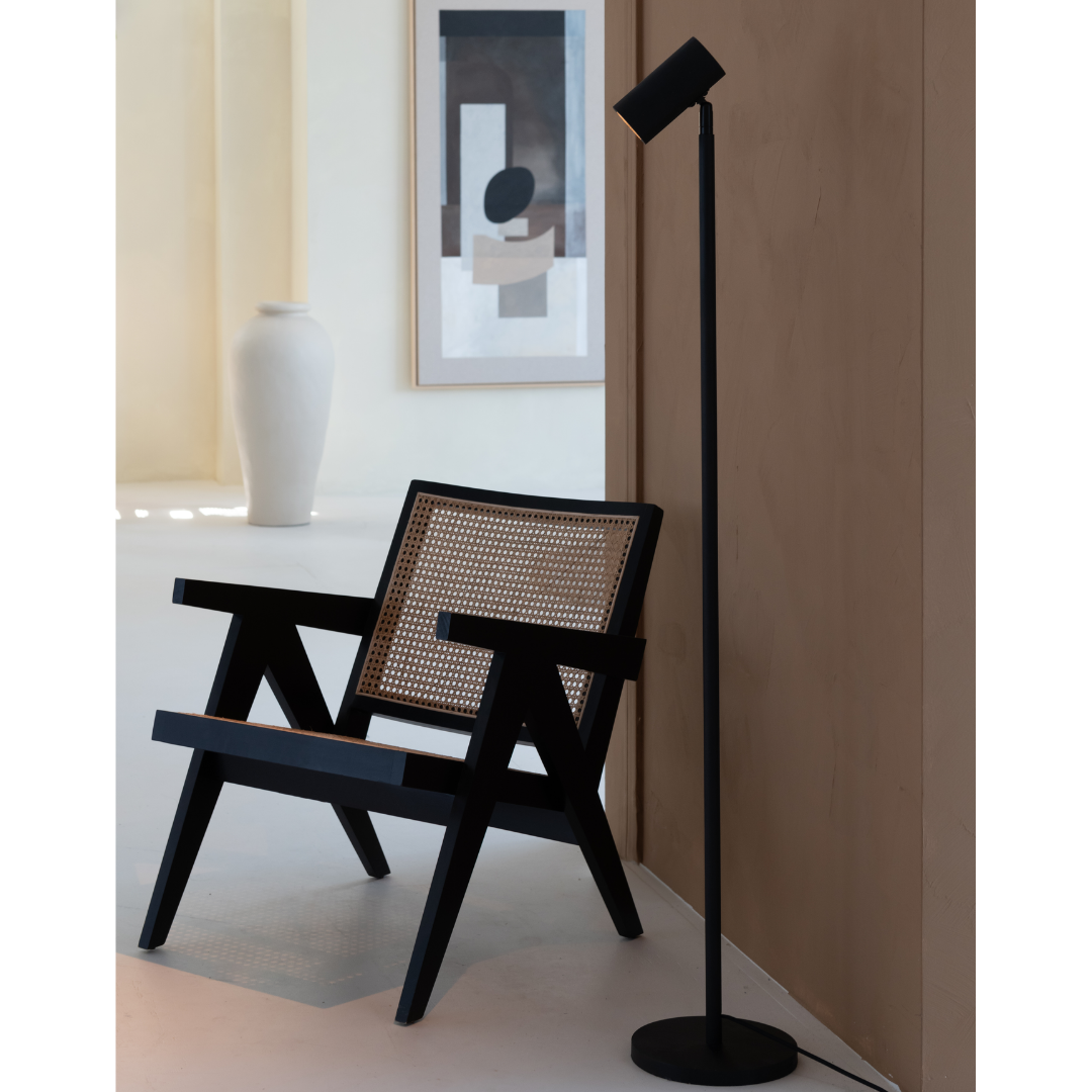 Ein Bild aus dem Taiga Store von taiga.green. Ein moderner schwarzer Holzstuhl mit Sitz und Rückenlehne aus geflochtenem Rohr sitzt neben einer hohen schwarzen Stehlampe an einer beigen Wand. Im Hintergrund schmücken eine weiße Vase und ein abstraktes Kunstwerk einen minimalistischen Raum. Jetzt bestellen im Eco Shop von www.taiga.green. Hier nachhaltig einkaufen mit dem Taiga Eco Rating