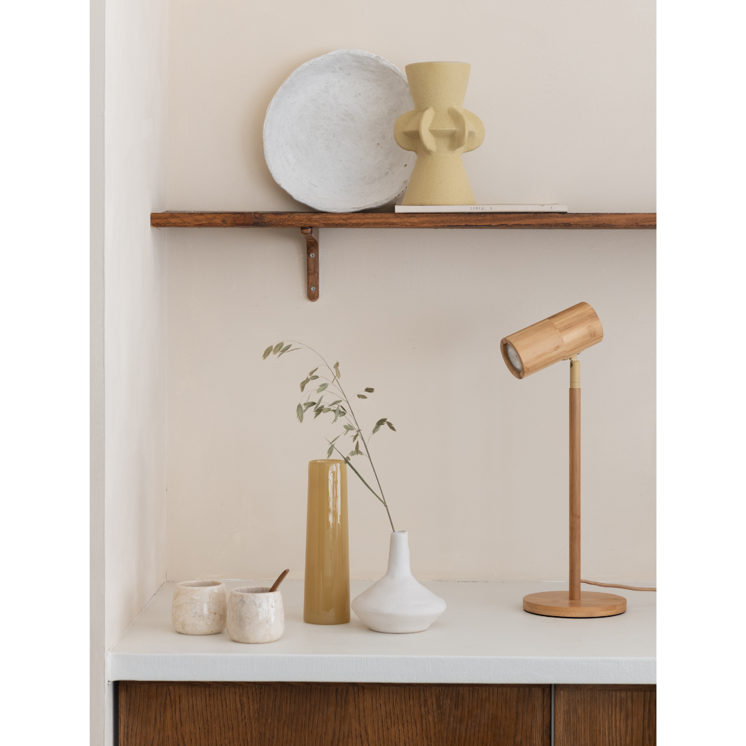 Ein Bild aus dem Taiga Store von taiga.green. Ein minimalistisch eingerichteter Schreibtisch mit einer Holzlampe, zwei Keramikbechern, einer gelben Vase mit Gras, einer weißen Vase und einem Holzschrank darunter. Auf einem Regal darüber stehen ein weißer Teller und eine gelbe Skulptur mit Struktur. Jetzt bestellen im Eco Shop von www.taiga.green. Hier nachhaltig einkaufen mit dem Taiga Eco Rating