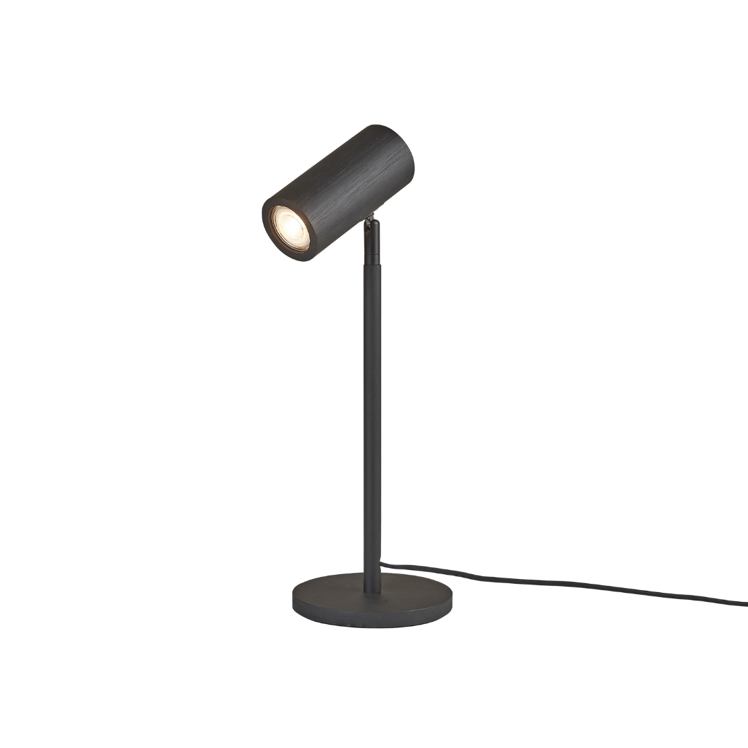Ein Bild aus dem Taiga Store von taiga.green. Eine moderne schwarze Schreibtischlampe mit einem zylindrischen, verstellbaren Kopf und einem schlanken, vertikalen Ständer auf einem runden Sockel, die eingeschaltet gezeigt wird, wobei eine sichtbare Schnur aus dem Sockel herausragt. Jetzt bestellen im Eco Shop von www.taiga.green. Hier nachhaltig einkaufen mit dem Taiga Eco Rating