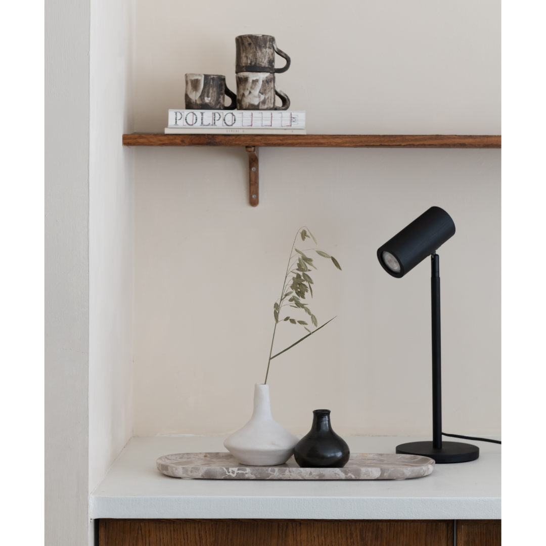 Ein Bild aus dem Taiga Store von taiga.green. Ein minimalistisches Regal mit gestapelten Tassen und Büchern befindet sich über einem weißen Tresen mit einem Tablett mit zwei Vasen, einem grünen Zweig und einer modernen schwarzen Schreibtischlampe vor einer neutralen Wand. Jetzt bestellen im Eco Shop von www.taiga.green. Hier nachhaltig einkaufen mit dem Taiga Eco Rating
