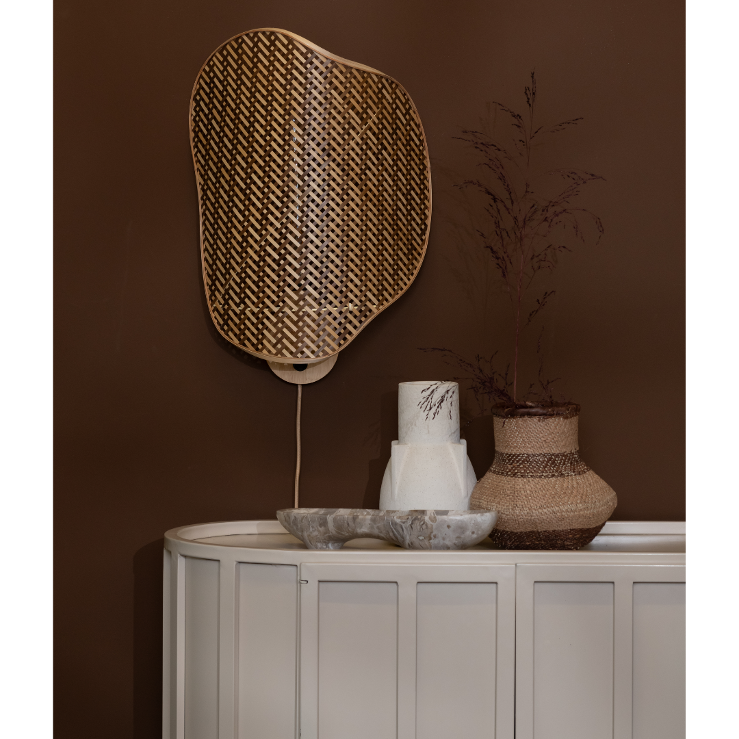 Ein Bild aus dem Taiga Store von taiga.green. Auf einem weißen Sideboard vor einer braunen Wand stehen ein geflochtener dekorativer Spiegel, eine Keramikvase, eine hohe strukturierte Vase mit getrockneten Zweigen und eine flache Marmorschale. Das Dekor hat eine moderne, erdige Ästhetik. Jetzt bestellen im Eco Shop von www.taiga.green. Hier nachhaltig einkaufen mit dem Taiga Eco Rating