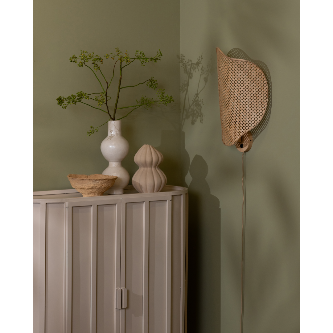 Ein Bild aus dem Taiga Store von taiga.green. Eine minimalistische Zimmerecke mit einem hellen Schrank, zwei dekorativen Vasen, einer kleinen Schale, einem belaubten Zweig in einer weißen Vase und einem Hut oder einer Lampe aus geflochtenem Rattan, die an einer gedämpften grünen Wand hängen. Jetzt bestellen im Eco Shop von www.taiga.green. Hier nachhaltig einkaufen mit dem Taiga Eco Rating