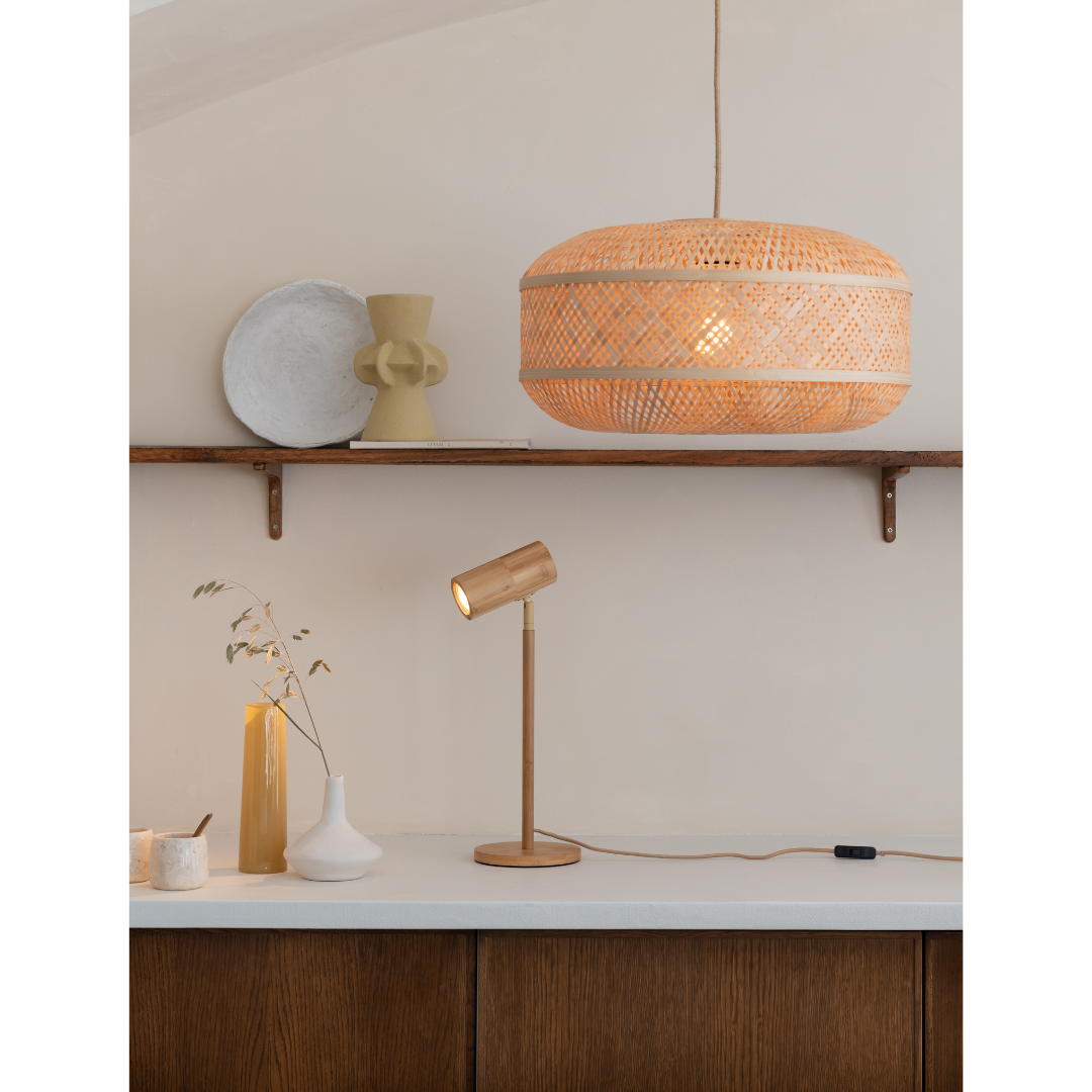 Ein Bild aus dem Taiga Store von taiga.green. Eine moderne, minimalistische Küche mit einem Holzschrank, einer weißen Arbeitsplatte und dekorativen Vasen. Darüber hängt eine geflochtene Hängelampe, die einen warmen Lichtschein abgibt. Eine Schreibtischlampe aus Metall steht auf dem Tresen unter einem rustikalen Holzregal. Jetzt bestellen im Eco Shop von www.taiga.green. Hier nachhaltig einkaufen mit dem Taiga Eco Rating