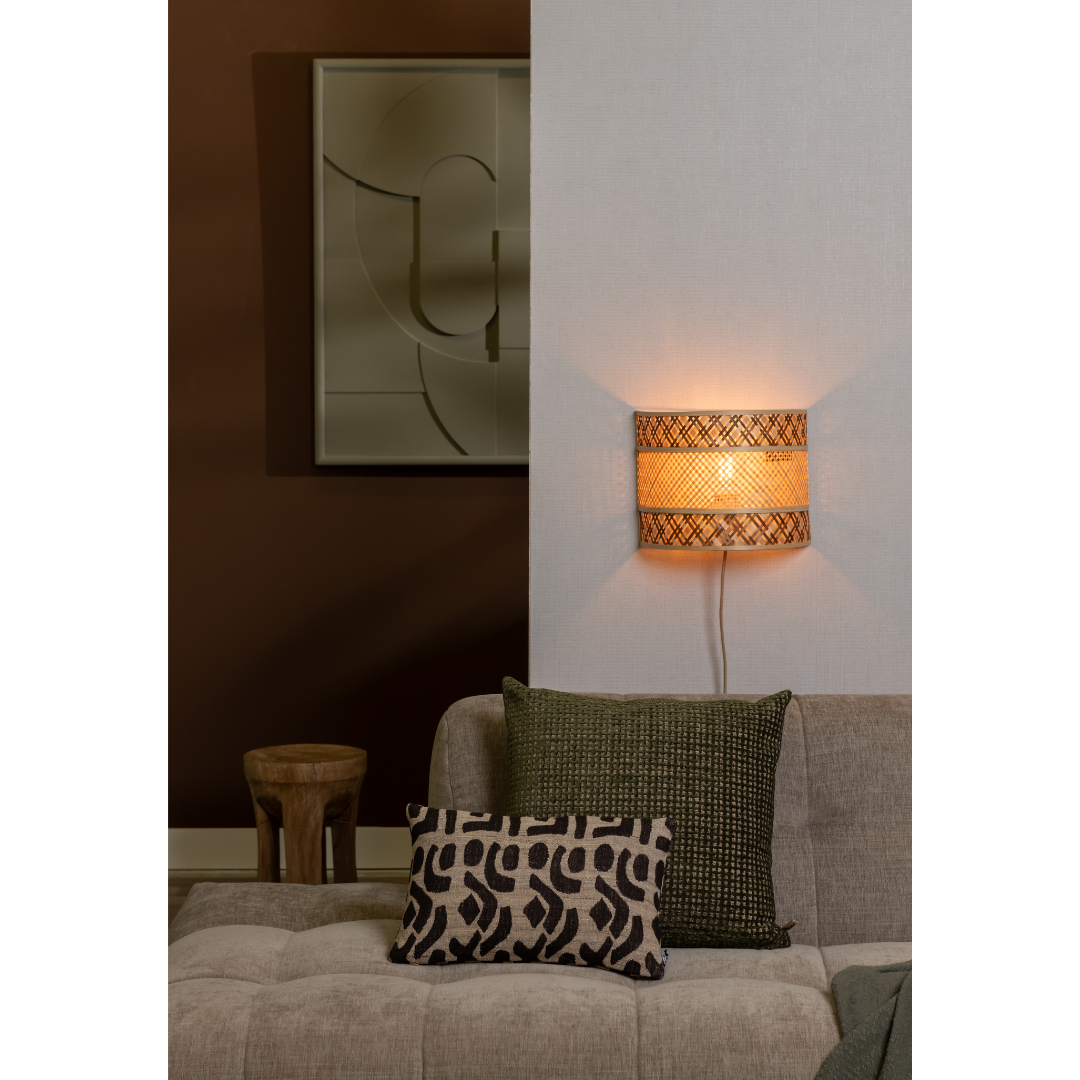 Ein Bild aus dem Taiga Store von taiga.green. Ein gemütliches Wohnzimmer mit einem beigen Sofa, zwei gemusterten Kissen, einer geflochtenen Wandlampe, die ein warmes Licht abgibt, einem kleinen Holzhocker und abstrakter Wandkunst vor einer halb braunen, halb hellen Wand. Jetzt bestellen im Eco Shop von www.taiga.green. Hier nachhaltig einkaufen mit dem Taiga Eco Rating