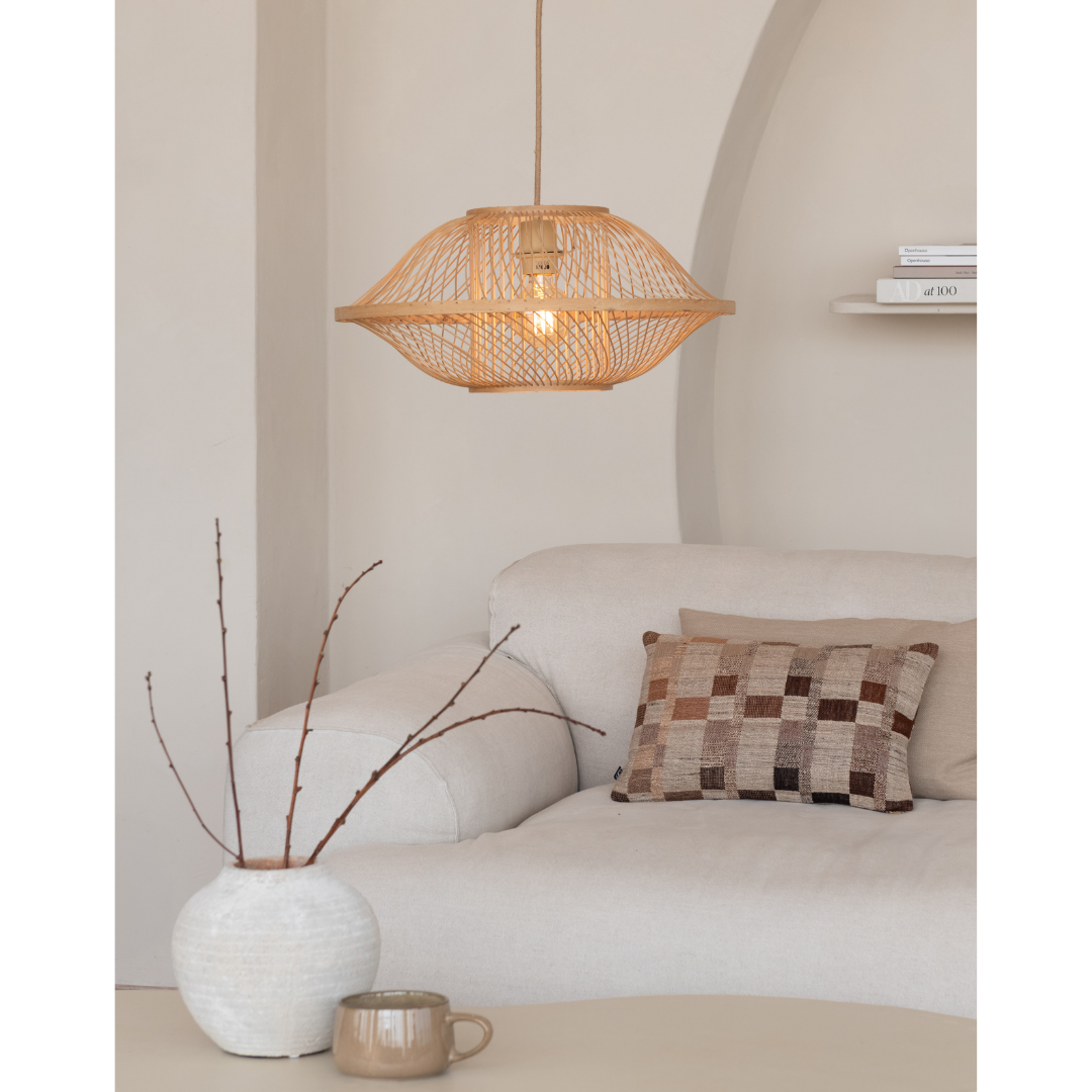 Ein Bild aus dem Taiga Store von taiga.green. Ein gemütliches Wohnzimmer mit einem hellbeigen Sofa, einem karierten braunen Kissen, einer weißen Vase mit kahlen Zweigen, einem Becher und der von der Decke hängenden geflochtenen Hängelampe Maui Bambus/Schirm S. In einem Wandregal stapeln sich Bücher. Jetzt bestellen im Eco Shop von www.taiga.green. Hier nachhaltig einkaufen mit dem Taiga Eco Rating
