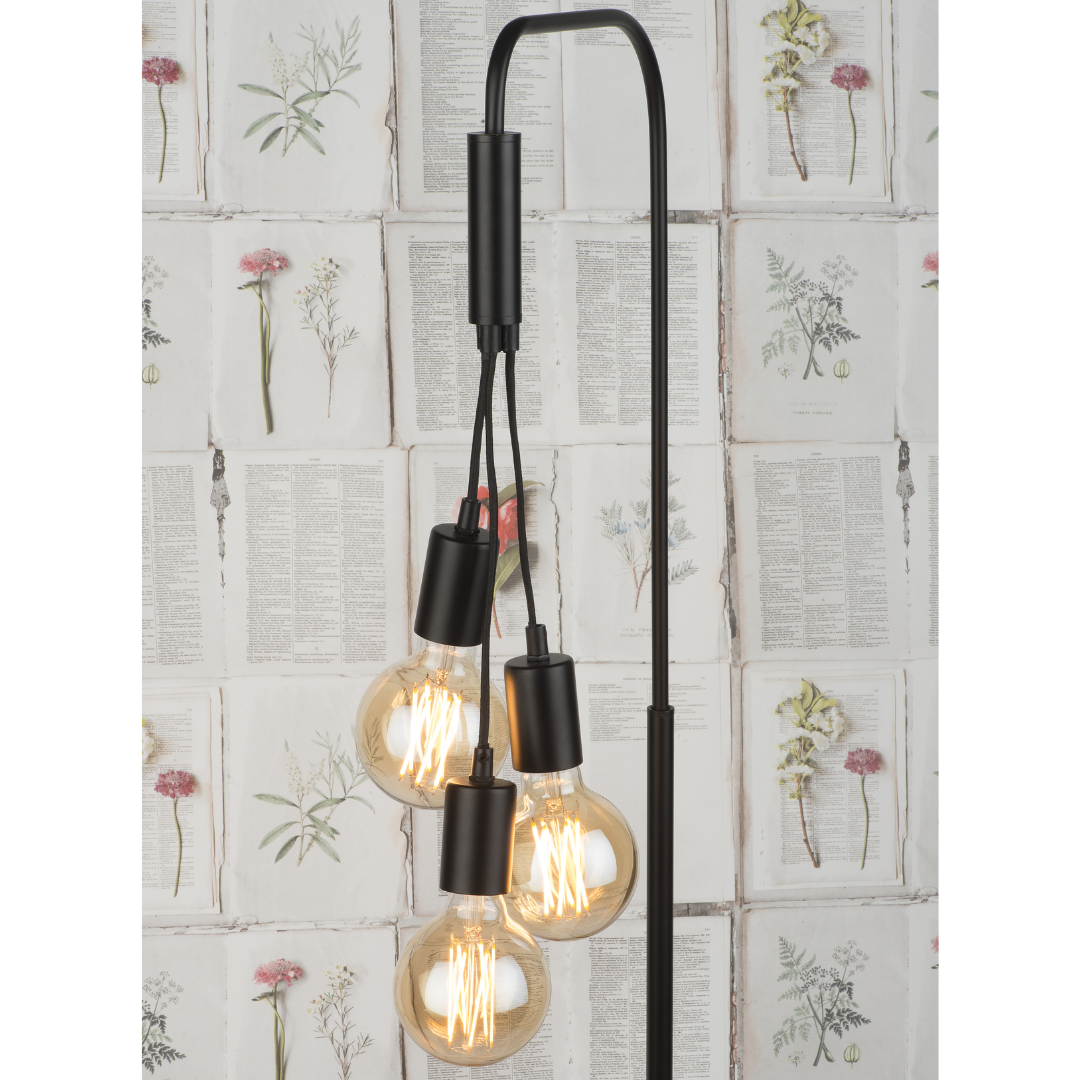 Ein Bild aus dem Taiga Store von taiga.green. Eine moderne schwarze Stehlampe mit vier freiliegenden Edison-Glühbirnen, die in verschiedenen Höhen hängen, vor einem Tapetenhintergrund mit botanischen Illustrationen und Textseiten. Jetzt bestellen im Eco Shop von www.taiga.green. Hier nachhaltig einkaufen mit dem Taiga Eco Rating