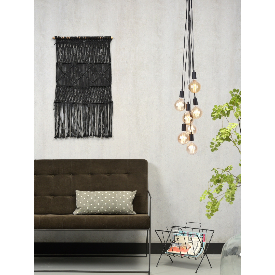 Ein Bild aus dem Taiga Store von taiga.green. Ein modernes Wohnzimmer mit einem dunklen Sofa, einem Polka-Dot-Kissen, einem schwarzen Makramee-Wandbehang, einer Reihe von Hängelampen, einer Pflanze und einem Zeitschriftenständer mit Magazinen. Jetzt bestellen im Eco Shop von www.taiga.green. Hier nachhaltig einkaufen mit dem Taiga Eco Rating