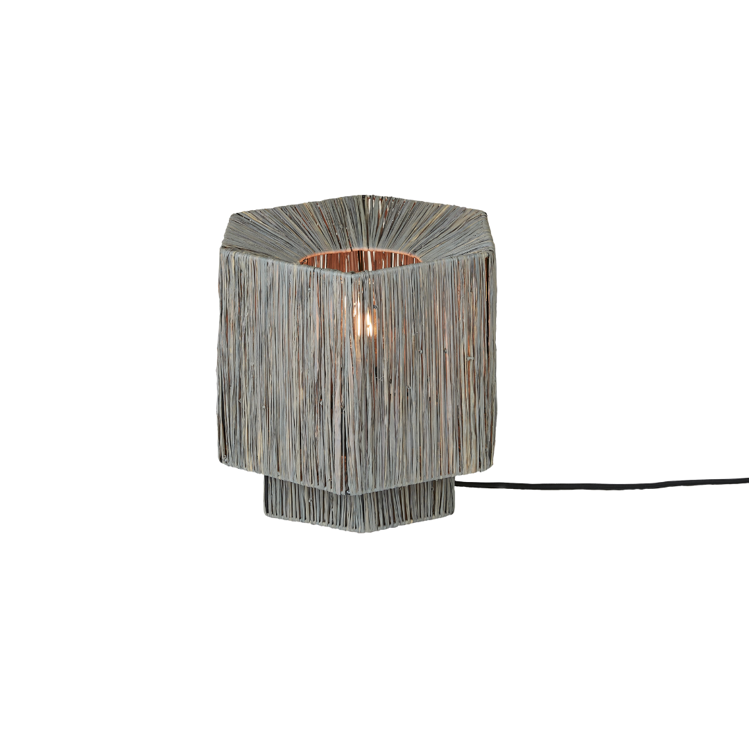 Ein Bild aus dem Taiga Store von taiga.green. Eine sechseckige Tischleuchte mit einem geflochtenen Drahtrahmen, der das Licht der Glühbirne im Inneren durch die dünnen, vertikalen Metallstränge scheinen lässt. Die Leuchte hat ein modernes und minimalistisches Design. Jetzt bestellen im Eco Shop von www.taiga.green. Hier nachhaltig einkaufen mit dem Taiga Eco Rating