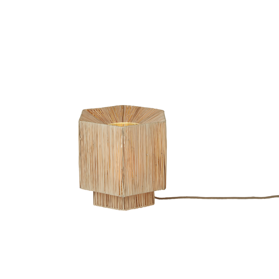Ein Bild aus dem Taiga Store von taiga.green. Eine kleine, sechseckige Tischlampe mit einem geflochtenen, strohähnlichen Schirm und Sockel. Die Lampe strahlt ein warmes Licht aus und hat eine sichtbare Schnur, die vom Sockel ausgeht. Jetzt bestellen im Eco Shop von www.taiga.green. Hier nachhaltig einkaufen mit dem Taiga Eco Rating
