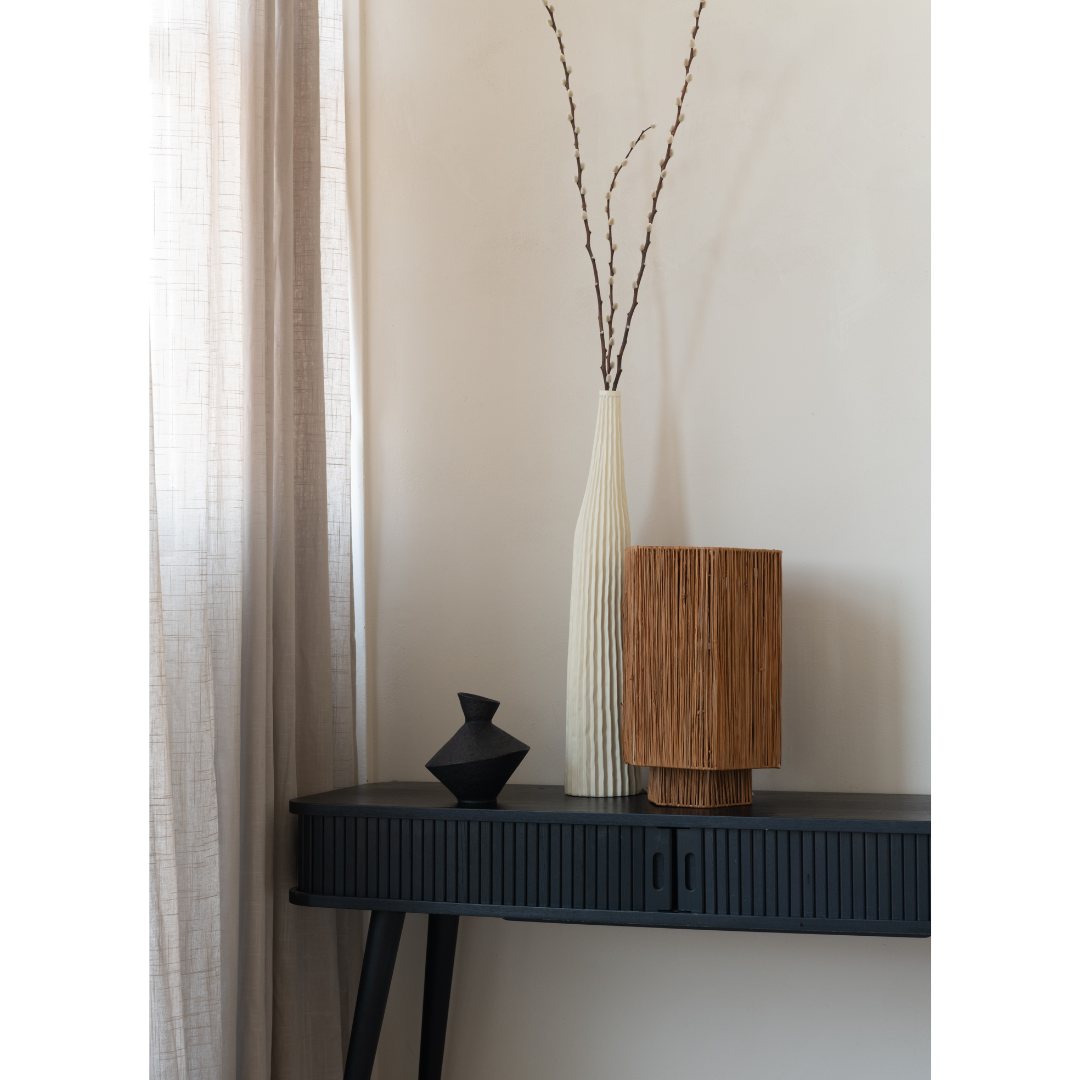 Ein Bild aus dem Taiga Store von taiga.green. Ein schwarzer Konsolentisch mit einer kleinen schwarzen Vase, eine hohe weiße strukturierte Vase mit Zweigen und eine zylindrische braune Lampe, die vor einer hellen Wand neben durchsichtigen beigen Vorhängen steht. Jetzt bestellen im Eco Shop von www.taiga.green. Hier nachhaltig einkaufen mit dem Taiga Eco Rating