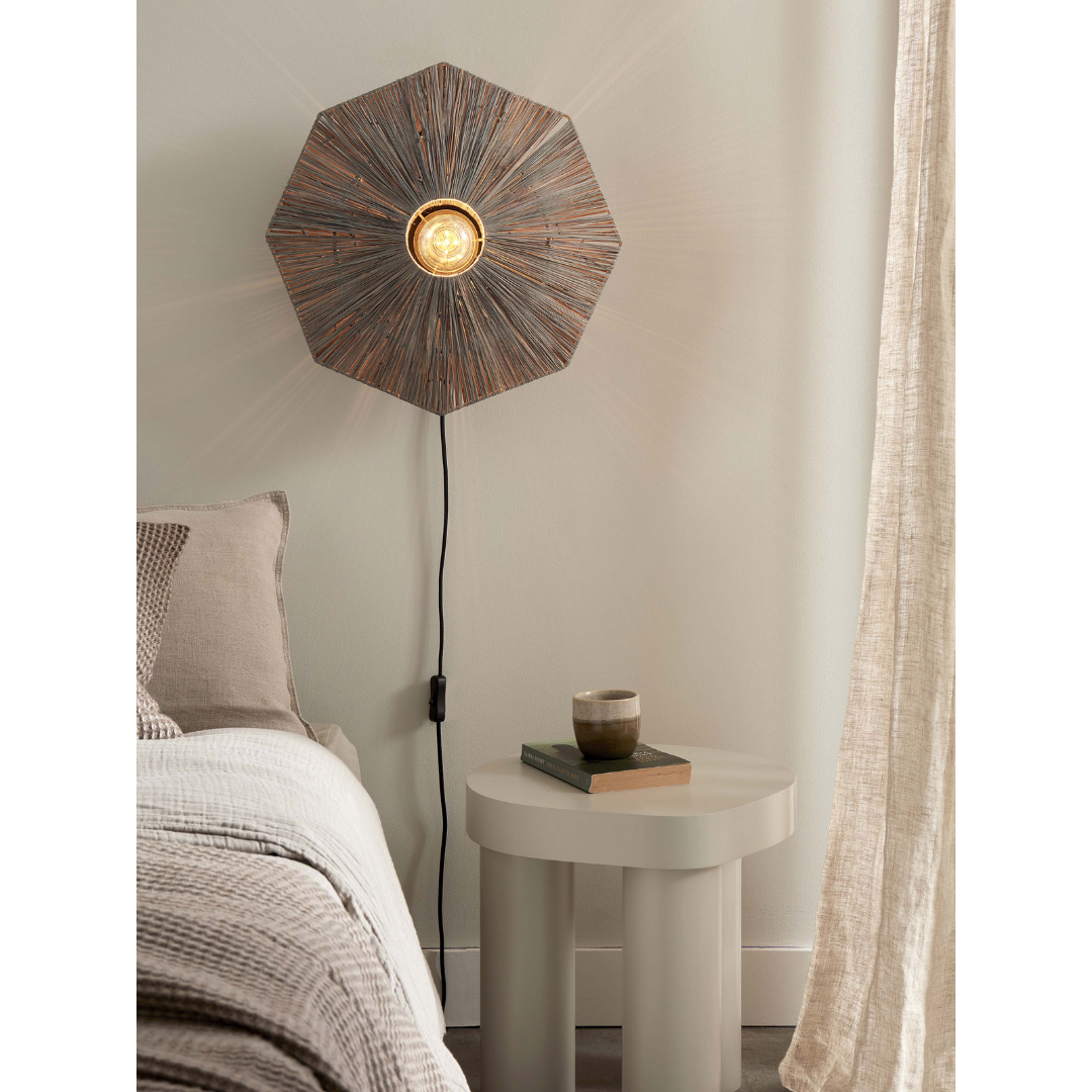 Ein Bild aus dem Taiga Store von taiga.green. Ein modernes Schlafzimmer mit einem beigen Bett, einem kleinen runden Beistelltisch, auf dem zwei Bücher und eine Tasse stehen, und einer geometrischen Wandlampe, die strahlendes Licht auf eine helle Wand neben den transparenten Vorhängen wirft. Jetzt bestellen im Eco Shop von www.taiga.green. Hier nachhaltig einkaufen mit dem Taiga Eco Rating