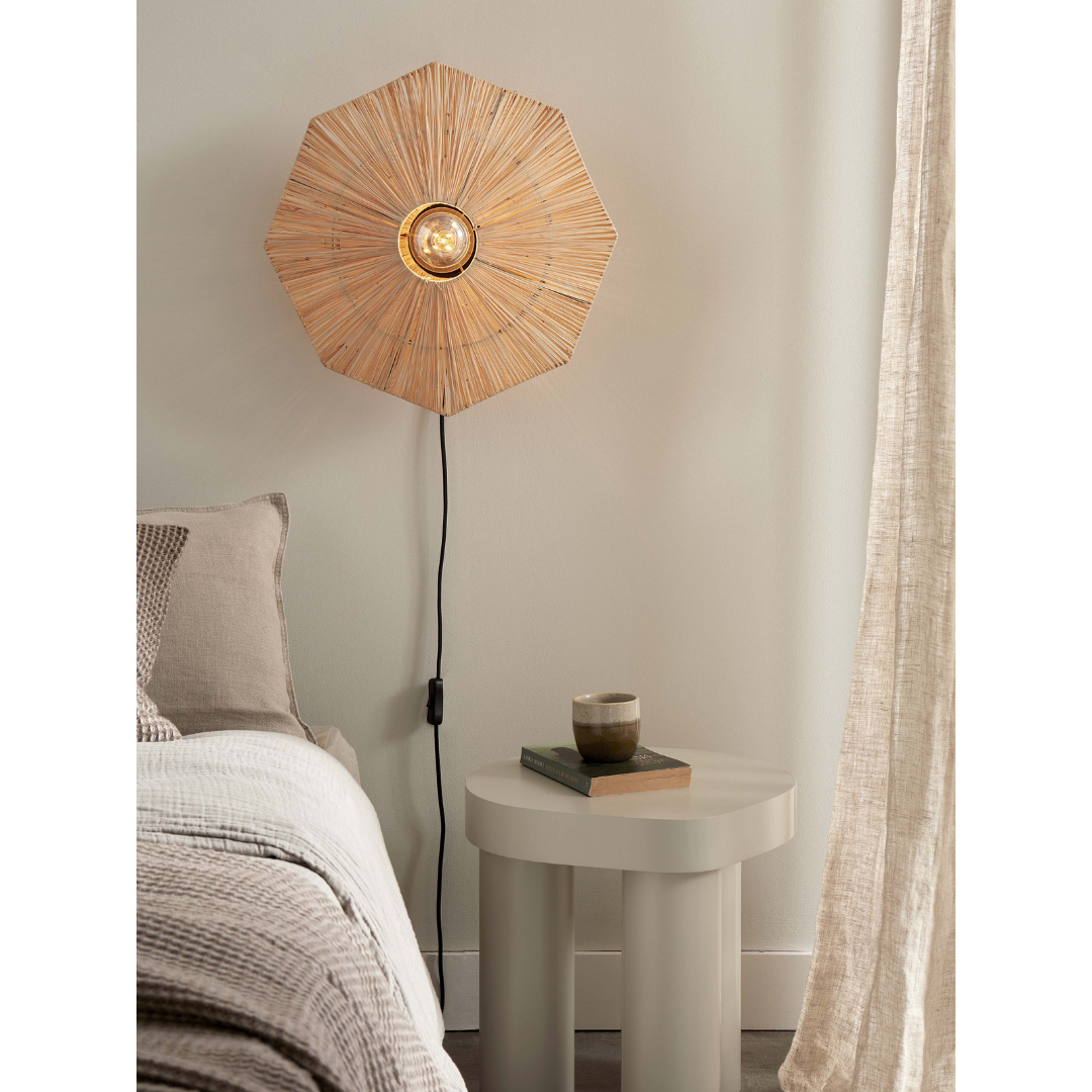 Ein Bild aus dem Taiga Store von taiga.green. Eine moderne Schlafzimmerecke mit einem Bett, einem runden Beistelltisch mit einer Tasse und einer Wandlampe mit einem geflochtenen Schirm im Sonnenschliff-Stil. Neutrale Töne und sanftes Sonnenlicht durch transparente Vorhänge schaffen eine gemütliche Atmosphäre. Jetzt bestellen im Eco Shop von www.taiga.green. Hier nachhaltig einkaufen mit dem Taiga Eco Rating