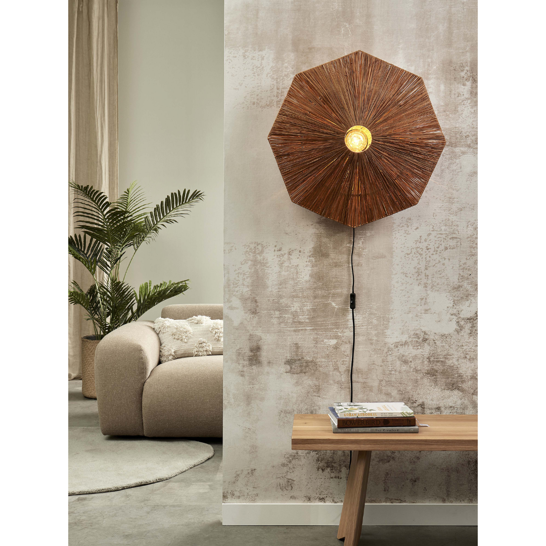 Ein Bild aus dem Taiga Store von taiga.green. Ein modernes Wohnzimmer mit einem großen, runden beigen Sofa, einer grünen Topfpflanze, einer Holzbank mit Büchern und einer Wandlampe mit einem braunen, geflochtenen, schirmförmigen Schirm vor einer strukturierten Wand. Jetzt bestellen im Eco Shop von www.taiga.green. Hier nachhaltig einkaufen mit dem Taiga Eco Rating