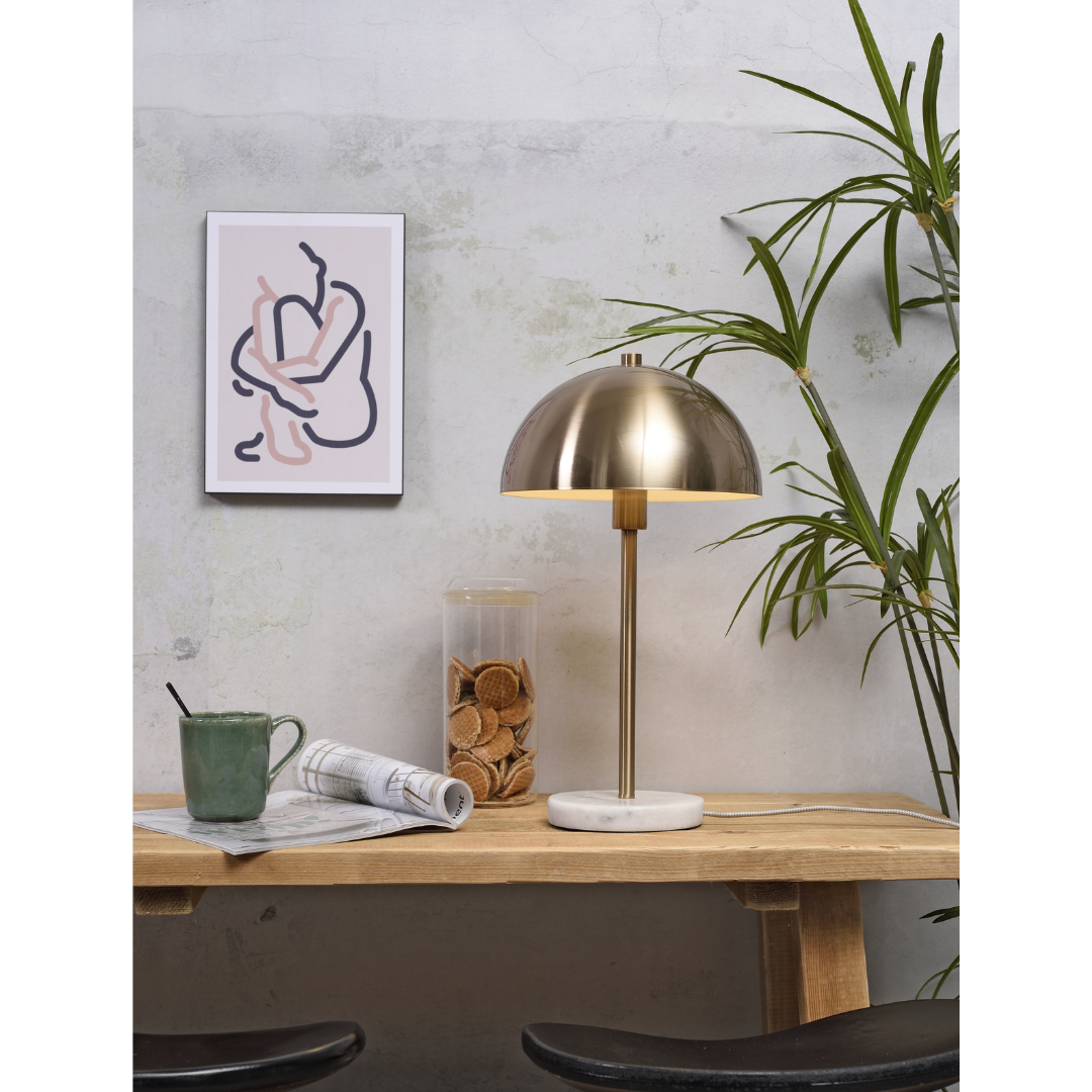 Ein Bild aus dem Taiga Store von taiga.green. Ein hölzerner Schreibtisch mit einer Messinglampe, einer grünen Tasse, einem Glas mit Keksen und einer zusammengerollten Zeitung. Eine Blattpflanze und abstrakte Kunst in einem weißen Rahmen stehen vor einer hellen, strukturierten Wand im Hintergrund. Jetzt bestellen im Eco Shop von www.taiga.green. Hier nachhaltig einkaufen mit dem Taiga Eco Rating