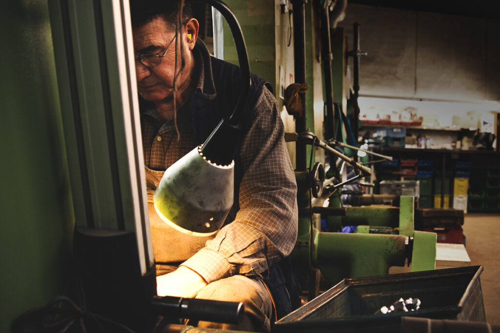 Ein Bild aus dem Taiga Store von taigagreen Ein Mann mit Brille konzentriert sich auf seine Arbeit an einer Maschine in einer Werkstatt Er wird von einer Deckenlampe beleuchtet und ist von verschiedenen grünen Maschinen umgeben Im Hintergrund sind Regale und Werkzeuge zu sehen Jetzt bestellen im Eco Shop von wwwtaigagreen Hier nachhaltig einkaufen mit dem Taiga Eco Rating