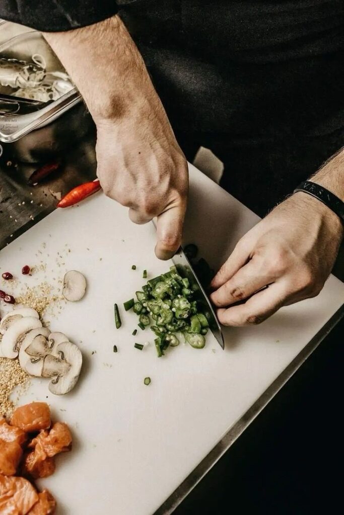 Ein Bild aus dem Taiga Store von taigagreen Eine Person schneidet mit einem Messer Frühlingszwiebeln auf einem weißen Schneidebrett Daneben liegen Pilzscheiben gehacktes Fleisch und eine Chilischote Die Person trägt ein dunkles Oberteil und ein Armband Jetzt bestellen im Eco Shop von wwwtaigagreen Hier nachhaltig einkaufen mit dem Taiga Eco Rating