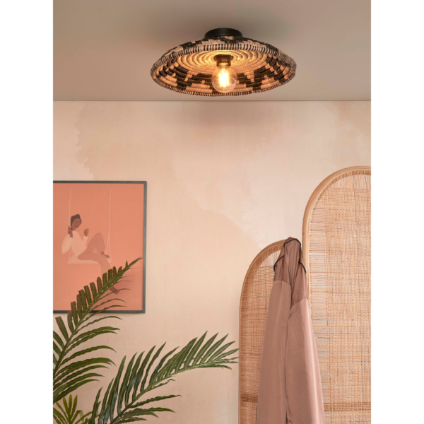 Ein Bild aus dem Taiga Store von taiga.green. Die Deckenlampe Andros Diam.45x8cm leuchtet warm über einem beigen Raum mit einem Rattantrenner, einer Blattpflanze, einem gerahmten Kunstwerk, das eine Person mit Hut zeigt, und einem beigen Mantel, der am Trenner hängt. Jetzt bestellen im Eco Shop von www.taiga.green. Hier nachhaltig einkaufen mit dem Taiga Eco Rating