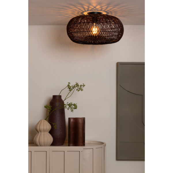 Ein Bild aus dem Taiga Store von taiga.green. Die Deckenlampe Arizona rattan/Schirm ø50x23cm S wirft Muster an die Decke über einem Schrank, der mit drei Vasen und Grünzeug geschmückt ist, während ein geometrisches Wandkunstwerk die angrenzende Wand ziert. Jetzt bestellen im Eco Shop von www.taiga.green. Hier nachhaltig einkaufen mit dem Taiga Eco Rating