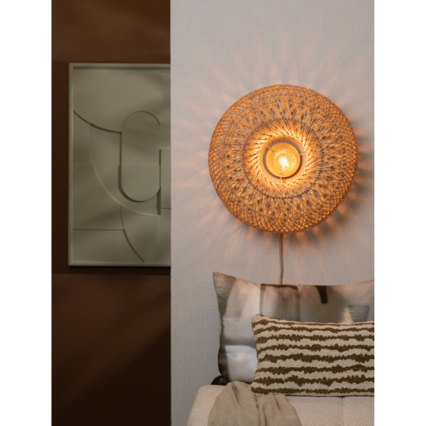 Ein Bild aus dem Taiga Store von taiga.green. Die Wandlampe Arizona rattan/Schirm ø50x23cm S strahlt ein warmes Licht aus und wirft gemusterte Schatten auf eine helle Wand über einem Sofa mit gemusterten Kissen. An der dunklen Wand daneben hängt ein abstraktes, gerahmtes Kunstwerk. Jetzt bestellen im Eco Shop von www.taiga.green. Hier nachhaltig einkaufen mit dem Taiga Eco Rating