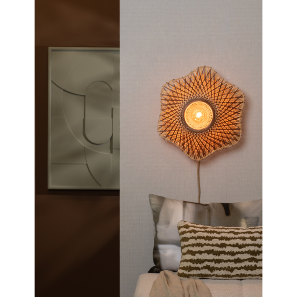 Ein Bild aus dem Taiga Store von taiga.green. Die Wandlampe Madura Bambus ø44x12cm S, eine geflochtene blumenförmige Wandlampe, leuchtet warm an einer hellen Wand über einem Sofa mit gemusterten Kissen. Ein abstraktes Kunstwerk schmückt die angrenzende, dunklere Wand. Jetzt bestellen im Eco Shop von www.taiga.green. Hier nachhaltig einkaufen mit dem Taiga Eco Rating