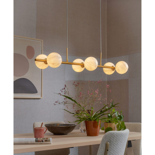 Ein Bild aus dem Taiga Store von taiga.green. Ein modernes Esszimmer mit einem hellen Holztisch, Topfpflanzen, einem rosa Becher und einer dekorativen Schale. Über dem Tisch hängt eine Pendelleuchte mit sechs leuchtenden Kugeln. An der Wand im Hintergrund ist abstrakte Kunst zu sehen. Jetzt bestellen im Eco Shop von www.taiga.green. Hier nachhaltig einkaufen mit dem Taiga Eco Rating