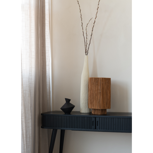 Ein Bild aus dem Taiga Store von taiga.green. Ein schwarzer Konsolentisch mit einer kleinen schwarzen Vase, eine hohe weiße strukturierte Vase mit Zweigen und eine zylindrische braune Lampe, die vor einer hellen Wand neben durchsichtigen beigen Vorhängen steht. Jetzt bestellen im Eco Shop von www.taiga.green. Hier nachhaltig einkaufen mit dem Taiga Eco Rating
