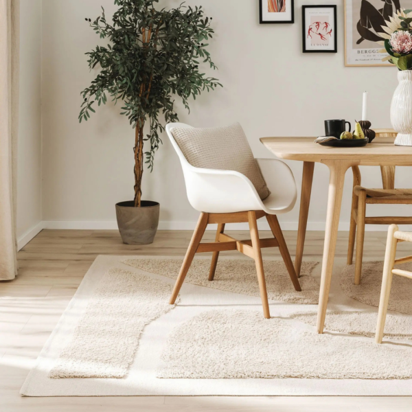 Ein Bild aus dem Taiga Store von taiga.green. Ein moderner Essbereich mit einem Holztisch, weißen und hölzernen Stühlen mit beigen Kissen, einer Topfpflanze, einem neutralen Teppich und Wandkunst an einer hellen Wand. Durch ein Fenster strömt Sonnenlicht herein. Jetzt bestellen im Eco Shop von www.taiga.green. Hier nachhaltig einkaufen mit dem Taiga Eco Rating